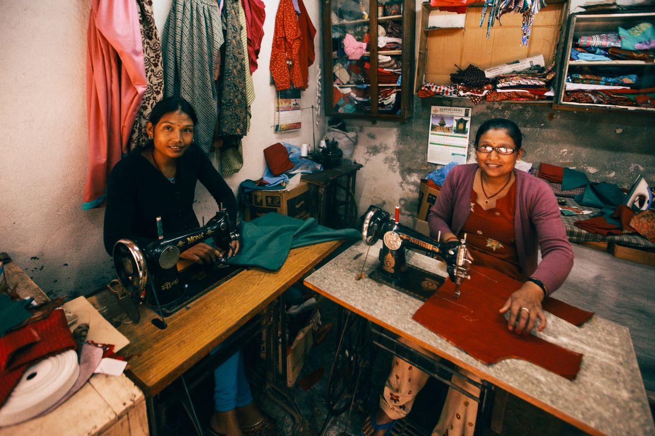 Two women sewing with vintage machines in a colorful dressmaking workshop, showcasing traditional skill.