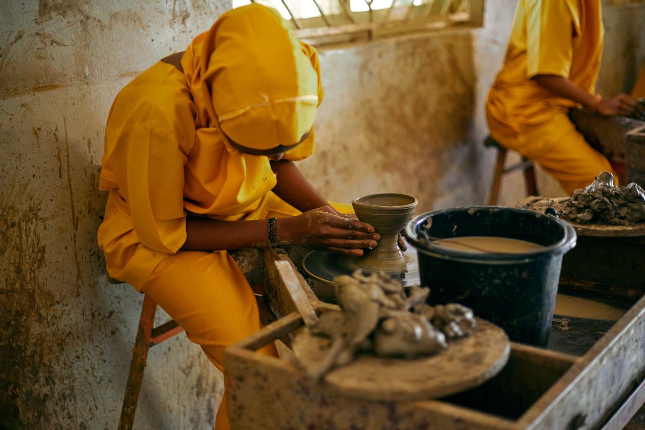 A woman in yellow is skillfully crafting pottery in a rustic workshop setting.