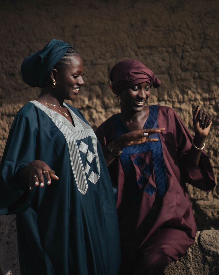Two women share a joyful moment in traditional African dresses outdoors.