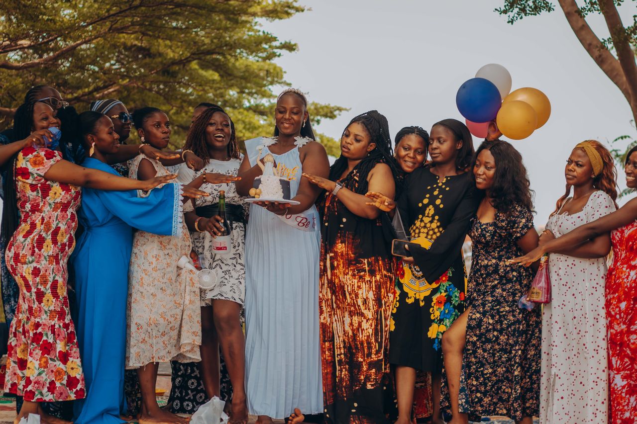 A joyful bridal shower with women celebrating outdoors, holding balloons and a cake.