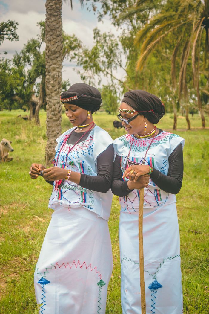 Two women wearing traditional African clothing standing in a green outdoor setting, embracing cultural heritage.