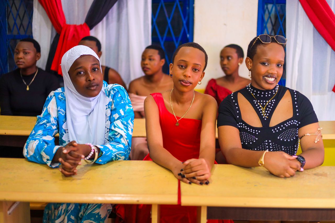 A group of young women in formal attire seated indoors, smiling and posing.